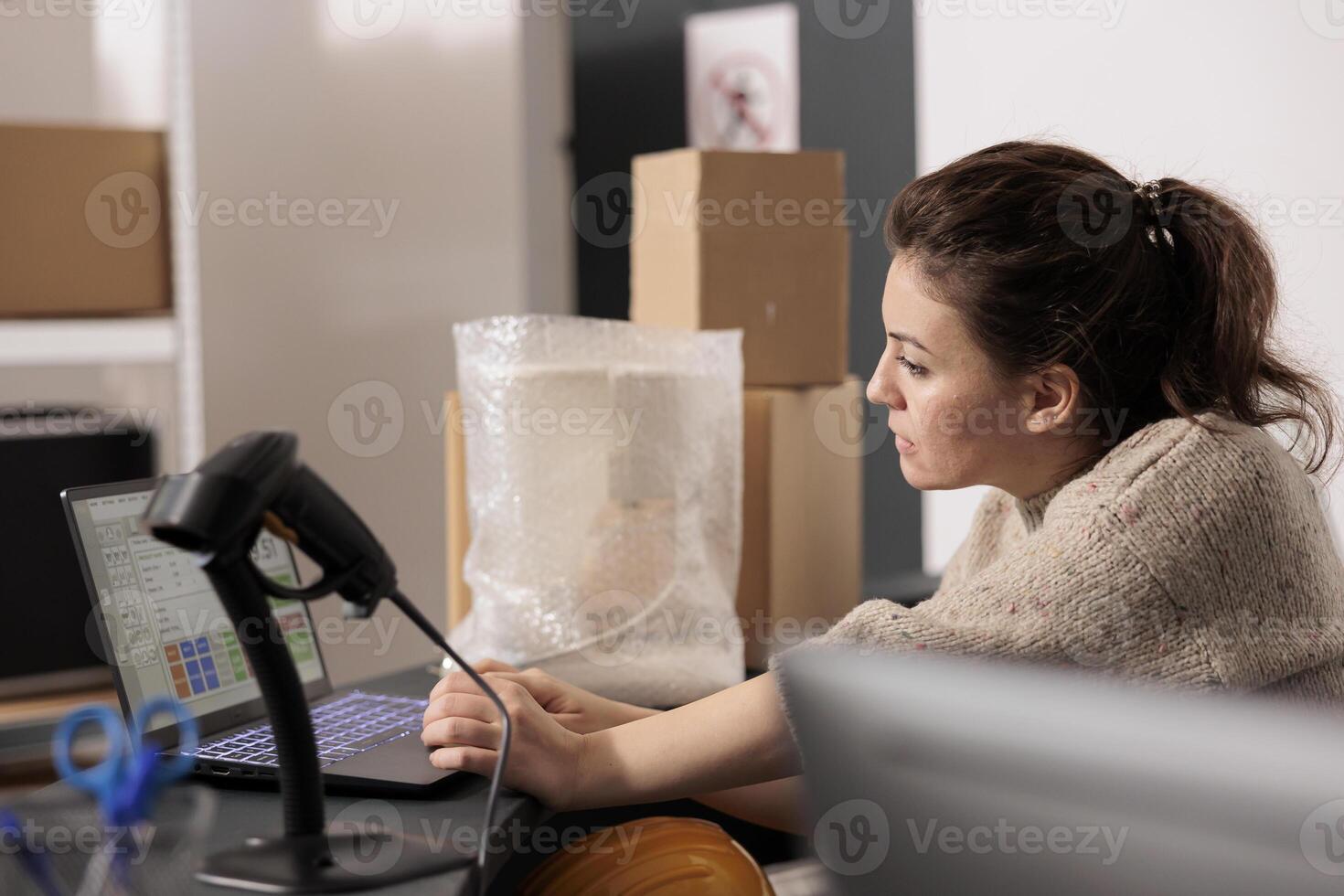 Stockroom supervisor standing at counter desk, analyzing merchandise logistics on computer. Storage room worker checking customers online orders preparing packages for delivery in storehouse photo