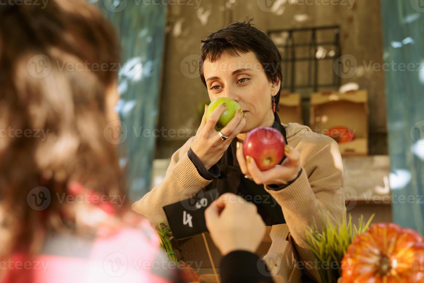 Selective focus of vendor smelling freshly harvested vibrant apples, helping client in selecting best product. Female supplier browsing locally grown bio produce, choosing for customer. photo