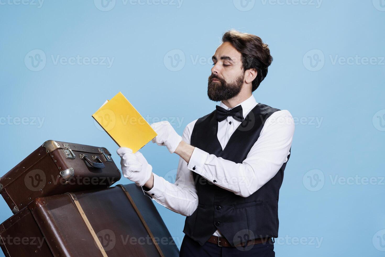 Clever porter reading poetry book on duty, feeling confident and enjoying literature or fiction. Young man acting as bellhop with passion for lecture studying novel story, hobby knowledge. photo