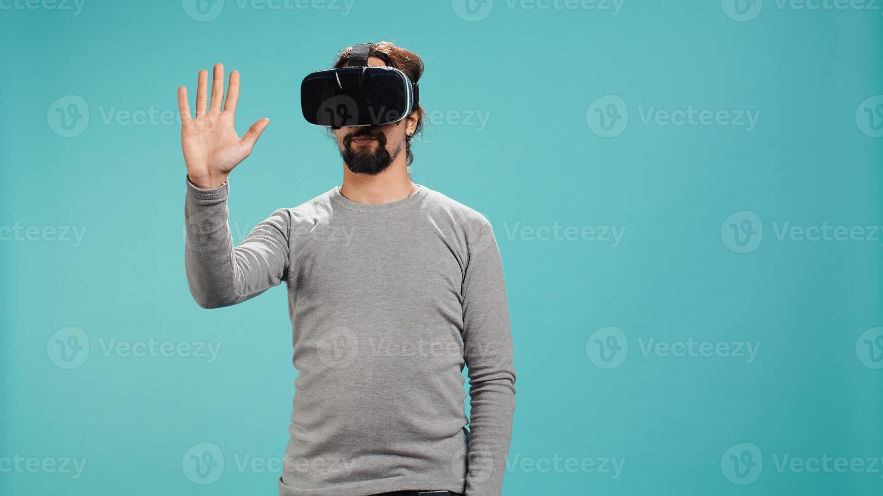 Tech enthusiast wearing virtual reality goggles, doing zooming in gestures. Arab man using high tech futuristic modern VR glasses, making tactile touching gesturing, studio background, camera B photo