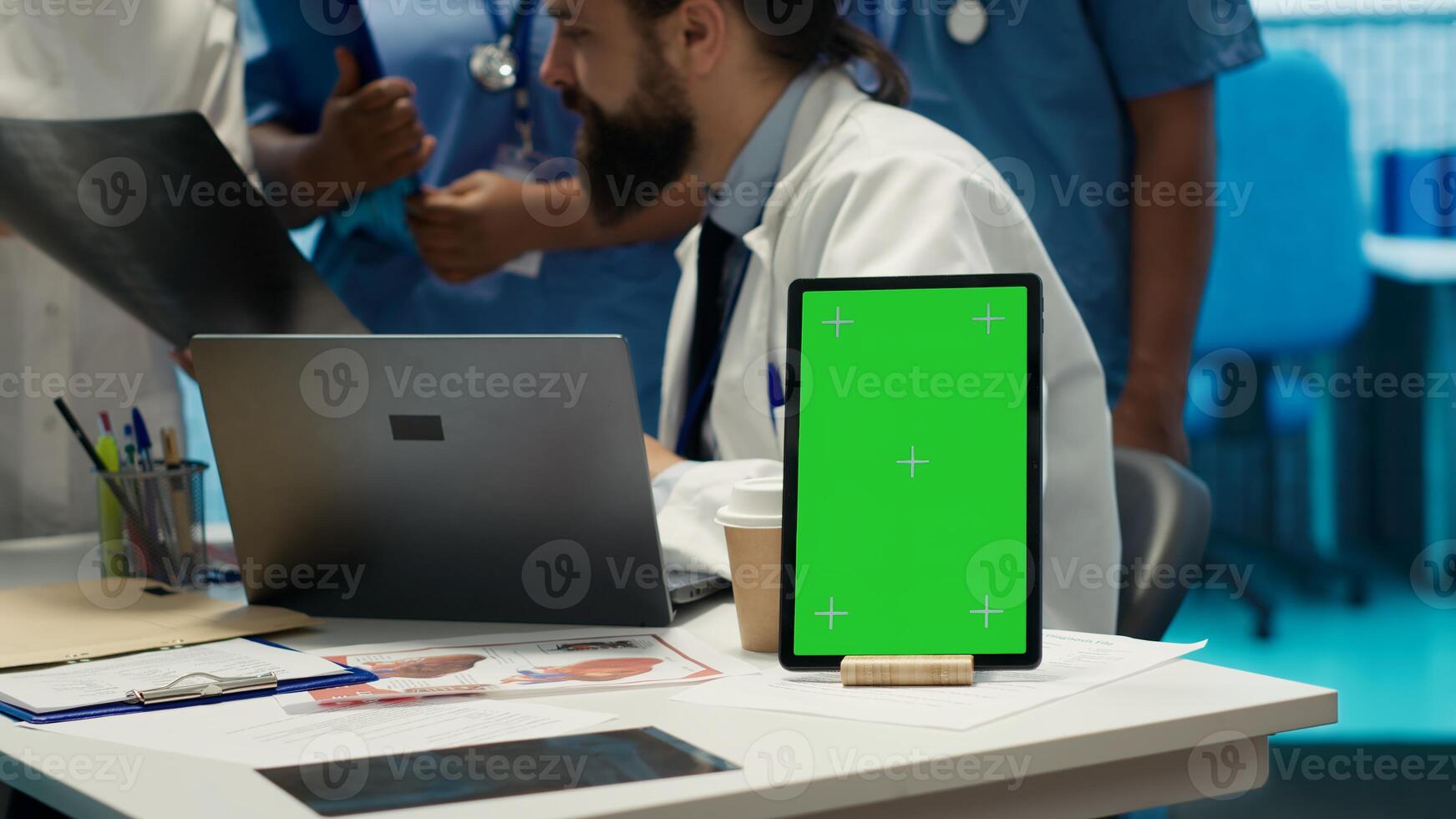 Team of doctors consulting analytics next to green screen on laptop in medical cabinet, examining x ray results to find the diagnosis. Licensed medics review hospital records at desk. Camera A. photo