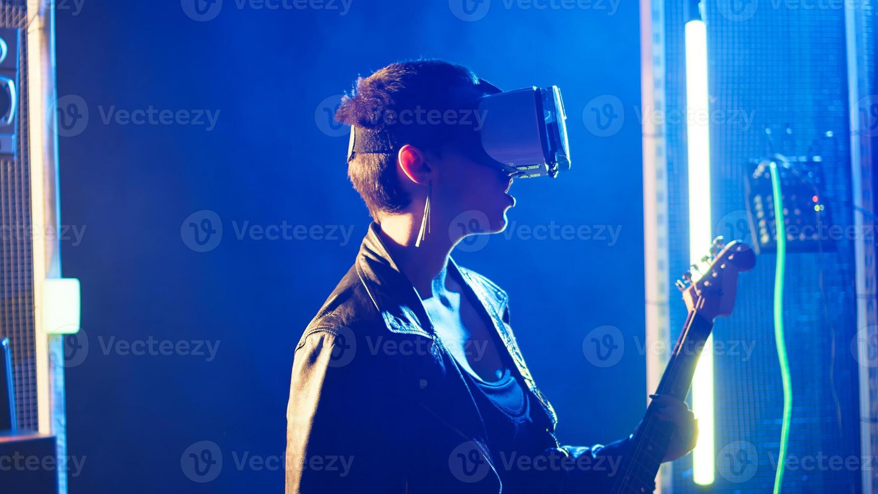Female musician using virtual reality headset during live show at nightclub, playing her electric guitar and wearing vr glasses. Woman rock star in leather does thrash metal. Camera A. photo