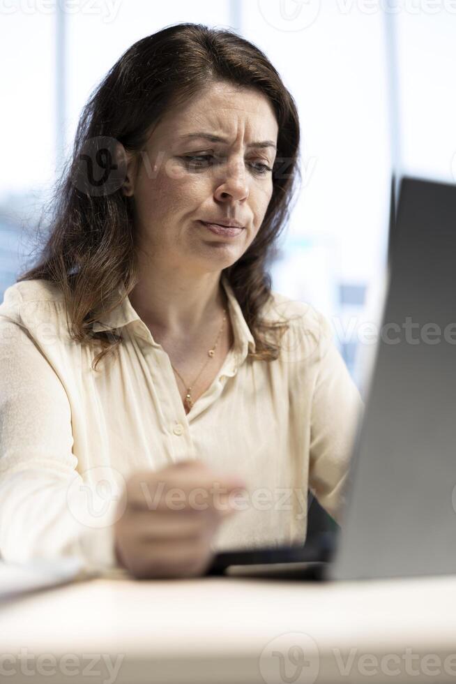 Overburdened entrepreneur in discomfort feeling tired and worried, working hard to meet deadline and protect her business. Young CEO being stressed and uncomfortable, overload. photo