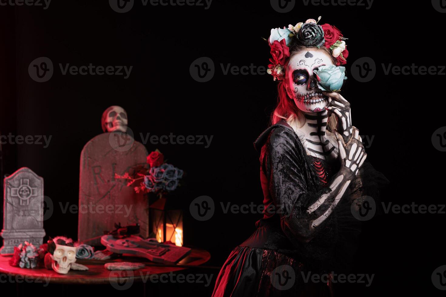 Sensual woman posing with blue rose for Day of the Dead Mexican celebration honoring dead loved ones. Seductive girl doing ancient Aztec custom of celebrating ancestors, wearing skull face paint photo