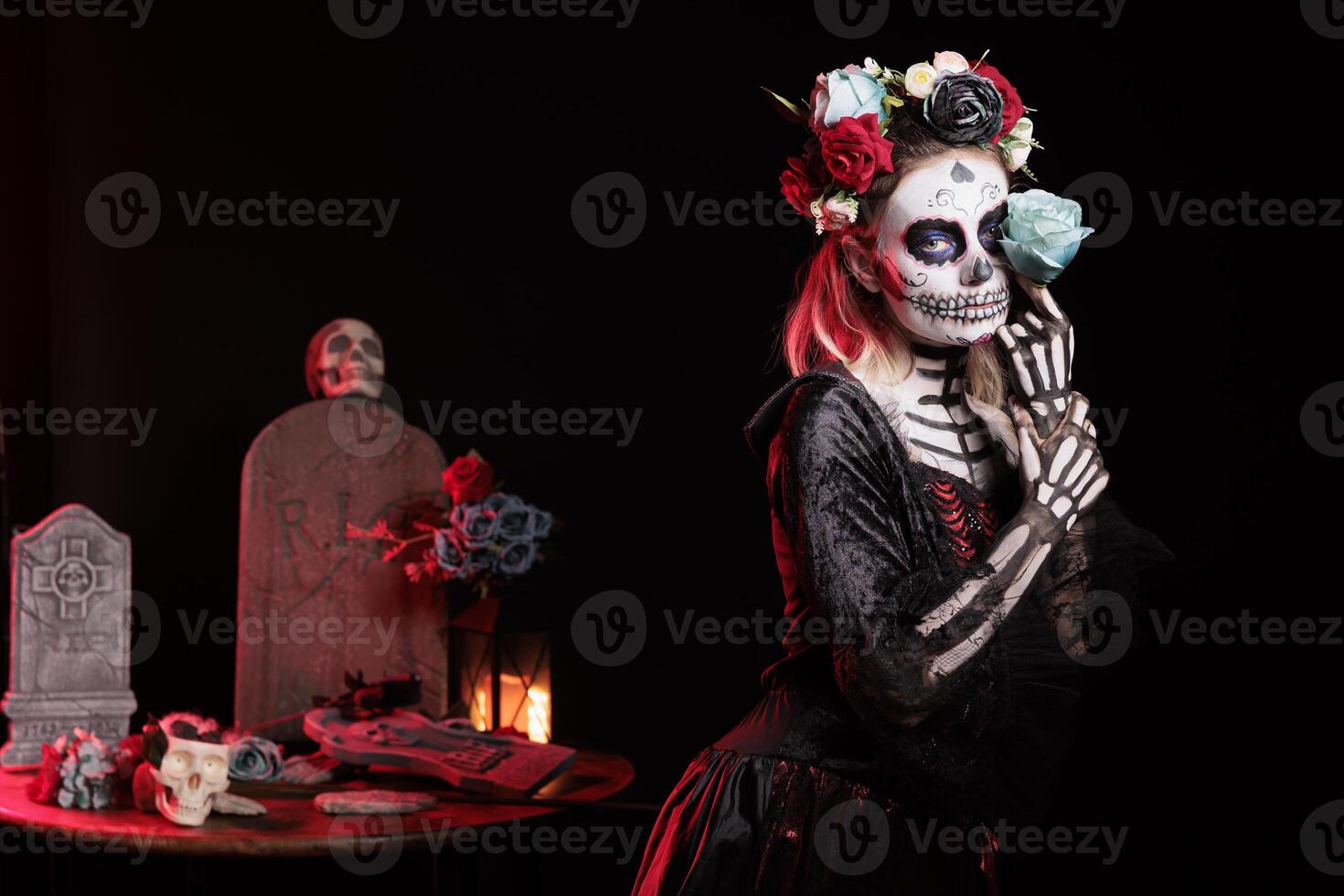 Woman doing sensual pose with rose in graveyard, celebrating Dia de los Muertos. Peculiar girl holding flower surrounded by frightening funeral items during Halloween horror event photo