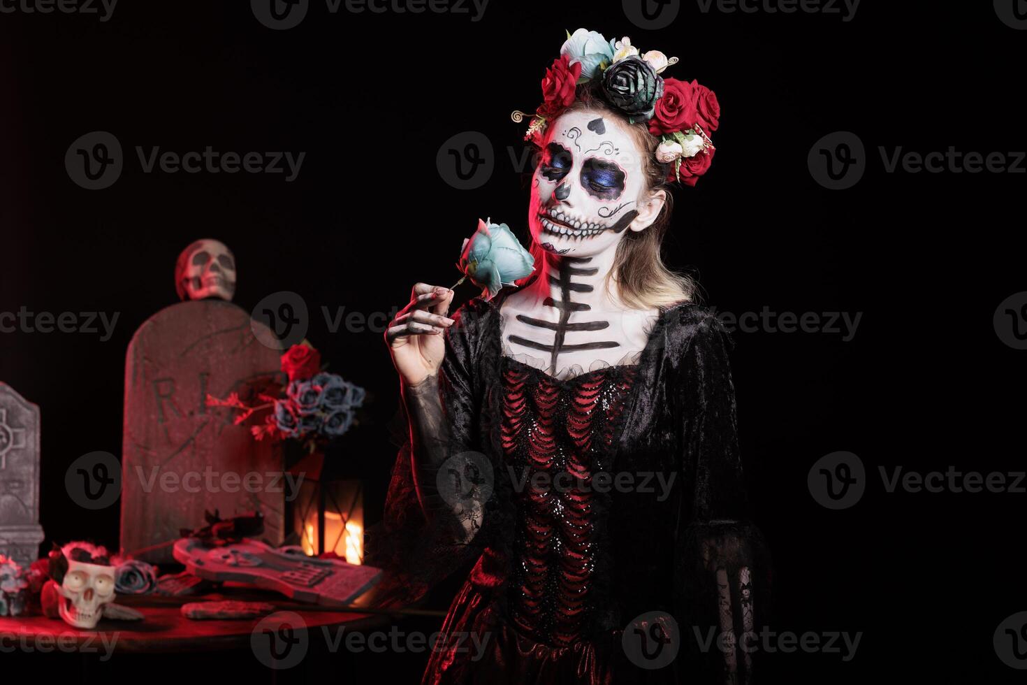 Girl smelling rose fragrance at Dia de los Muertes indigenous rites of honoring the dead. Woman enjoying flower scent aroma participating in Day of the Dead celebration in honor of the deceased photo