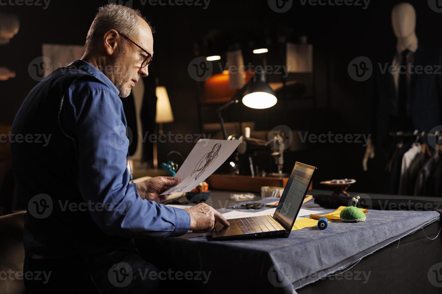 Experienced elderly tailor checking customer appointment schedule list before starting customization comission in atelier shop studio. Dressmaker working with sartorial outfit design sketch drawing photo