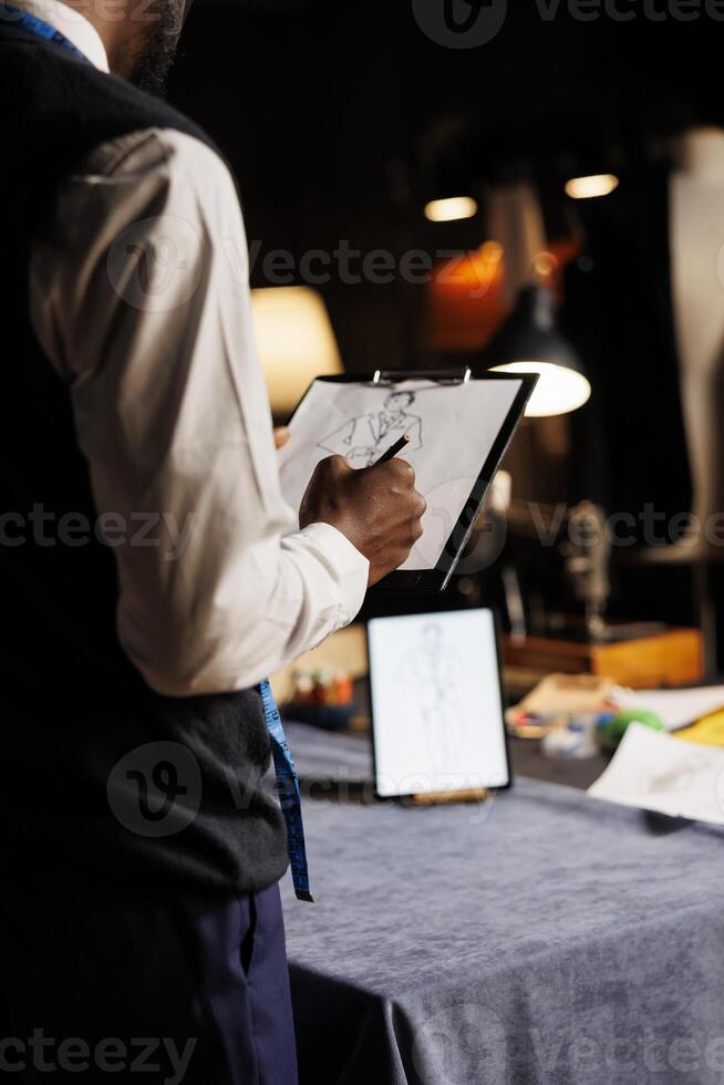 Meticulous fashion designer conceptualizing bespoke sartorial business suit collection in tailoring studio. Creative suitmaker handdrawing sketch of custom made garment piece photo
