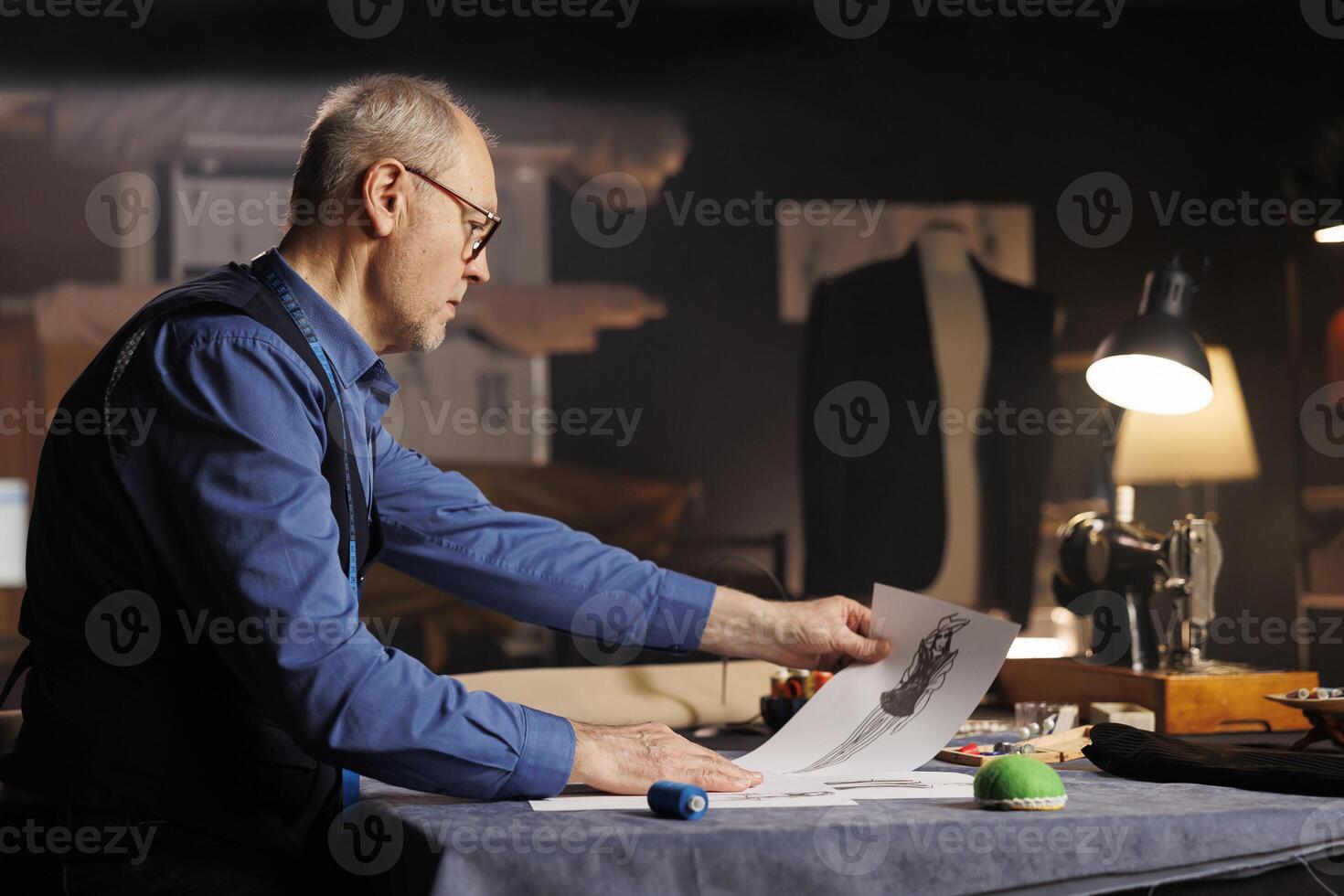 Creative elderly fashion designer creating outfits for upcoming fashion runway show project, conceptualizing different garment combinations using sketch drawings in tailoring studio photo