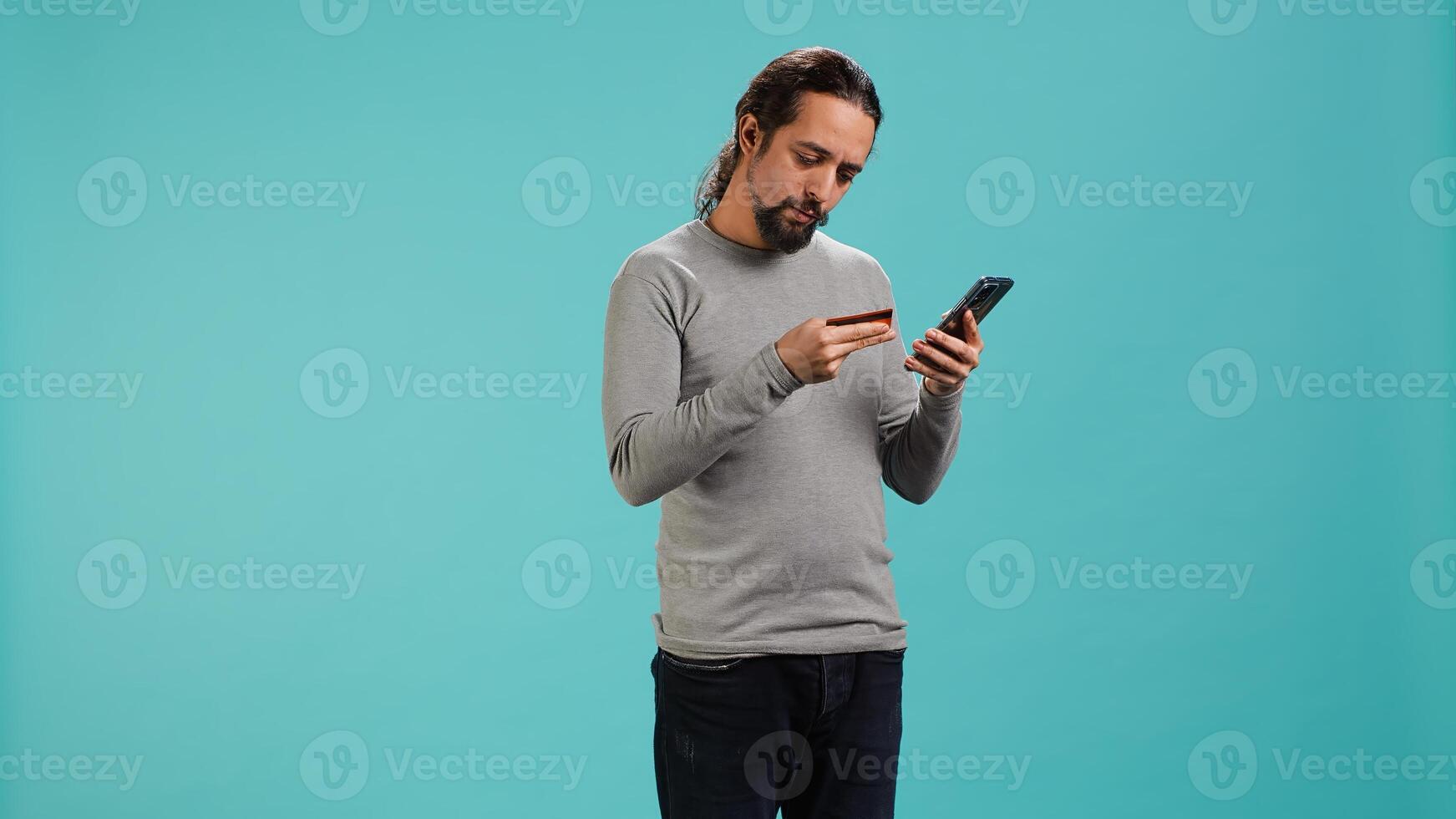 Elated man adding payment method on website, delighted to take advantage of promotions, studio background. Joyful person thrilled to do internet shopping, typing credit card data on phone, camera A photo