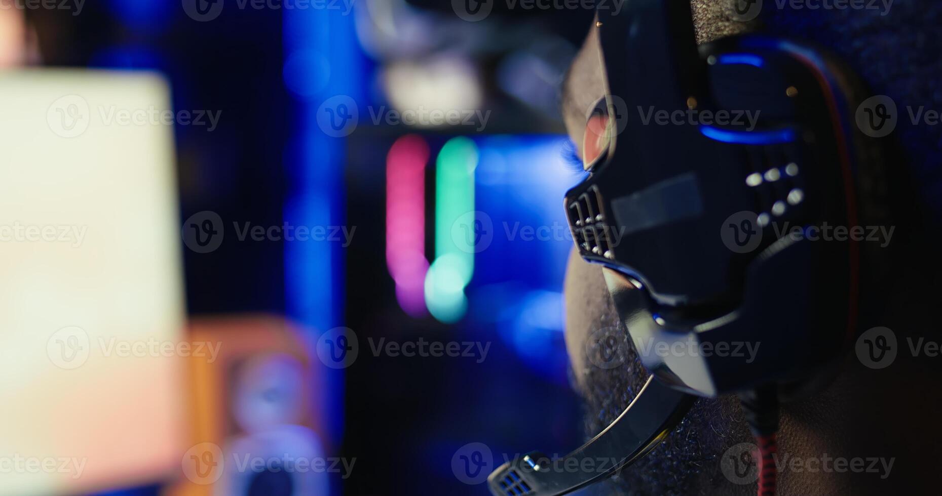 Man playing SF videogame on computer, having fun in neon lit apartment, close up. Gamer competing in online multiplayer game, using headphones to talk with teammates, camera B photo