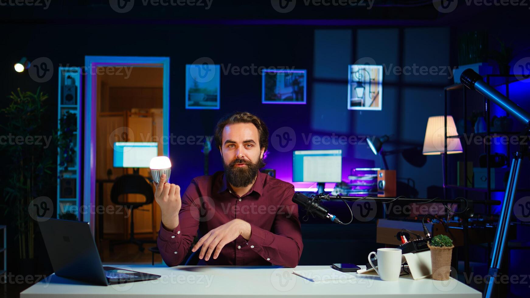 Tech guru in dimly lit apartment studio filming smart light bulb review for online streaming platforms. Media star hosting show, presenting IoT home automation product, camera B photo