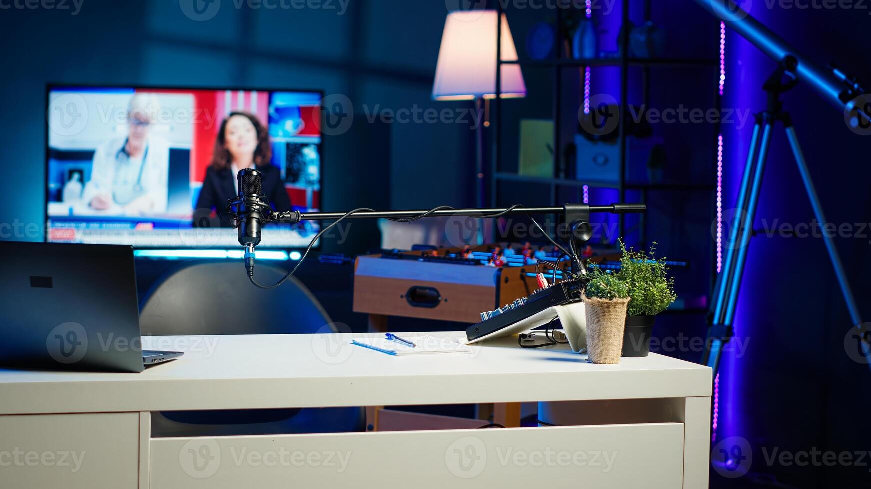 Panning shot of empty home studio illuminated with neon lights used for internet production. Living room filled with content creation equipment, TV animations running in background photo