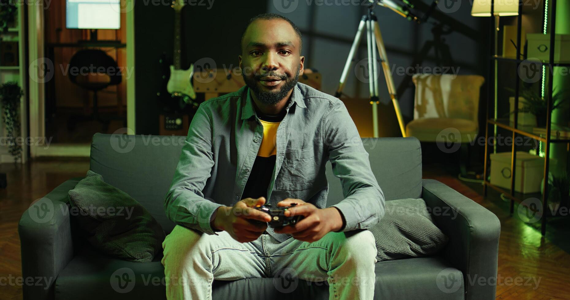 Fatigued player in RGB lit home late at night gaming with gamepad. Sleepy person sitting on sofa in neon illuminated apartment, playing videogames on console, looking exhausted, camera B photo