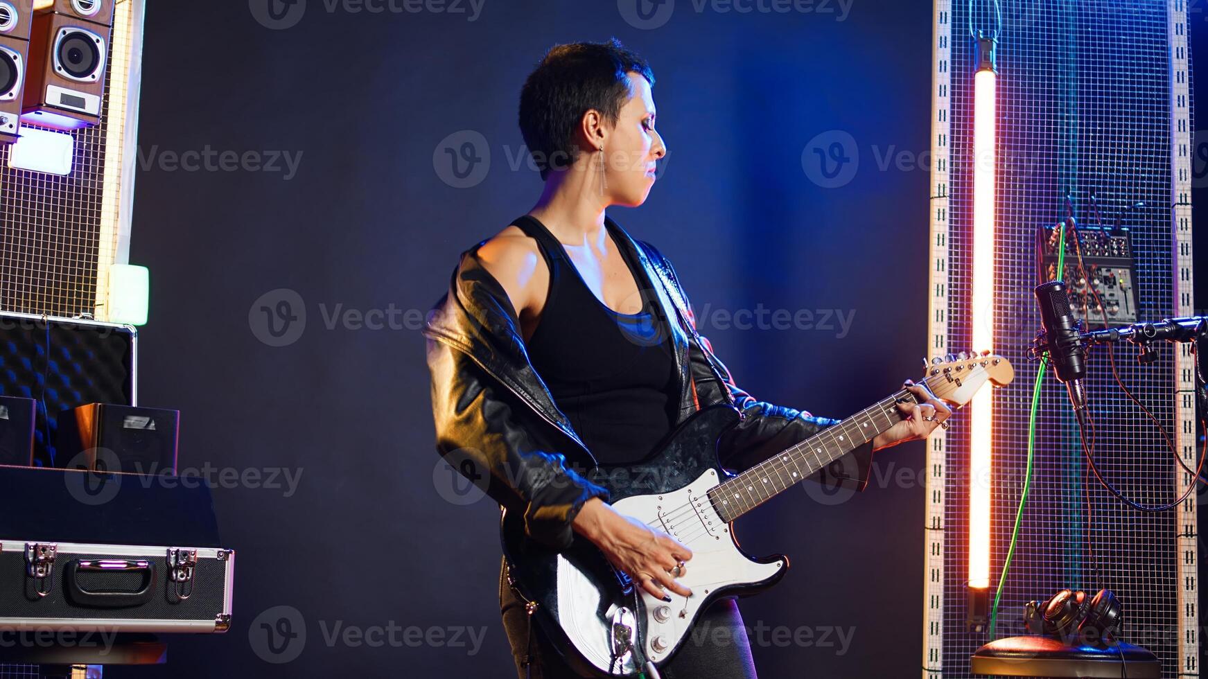 Woman performer showing thumbs up symbol and playing guitar, edgy grunge music performance in studio. Female rocker artist giving her approval with a positive like sign. Camera A. photo