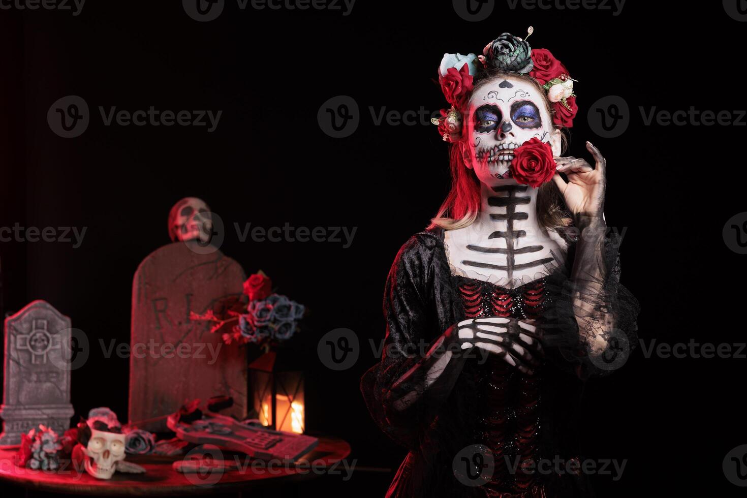 Dark lady posing with red rose during Dia de los Muertos, preserving cultural traditions between generations. Woman wearing la Catrina costume and skull makeup to celebrate Mexican culture photo
