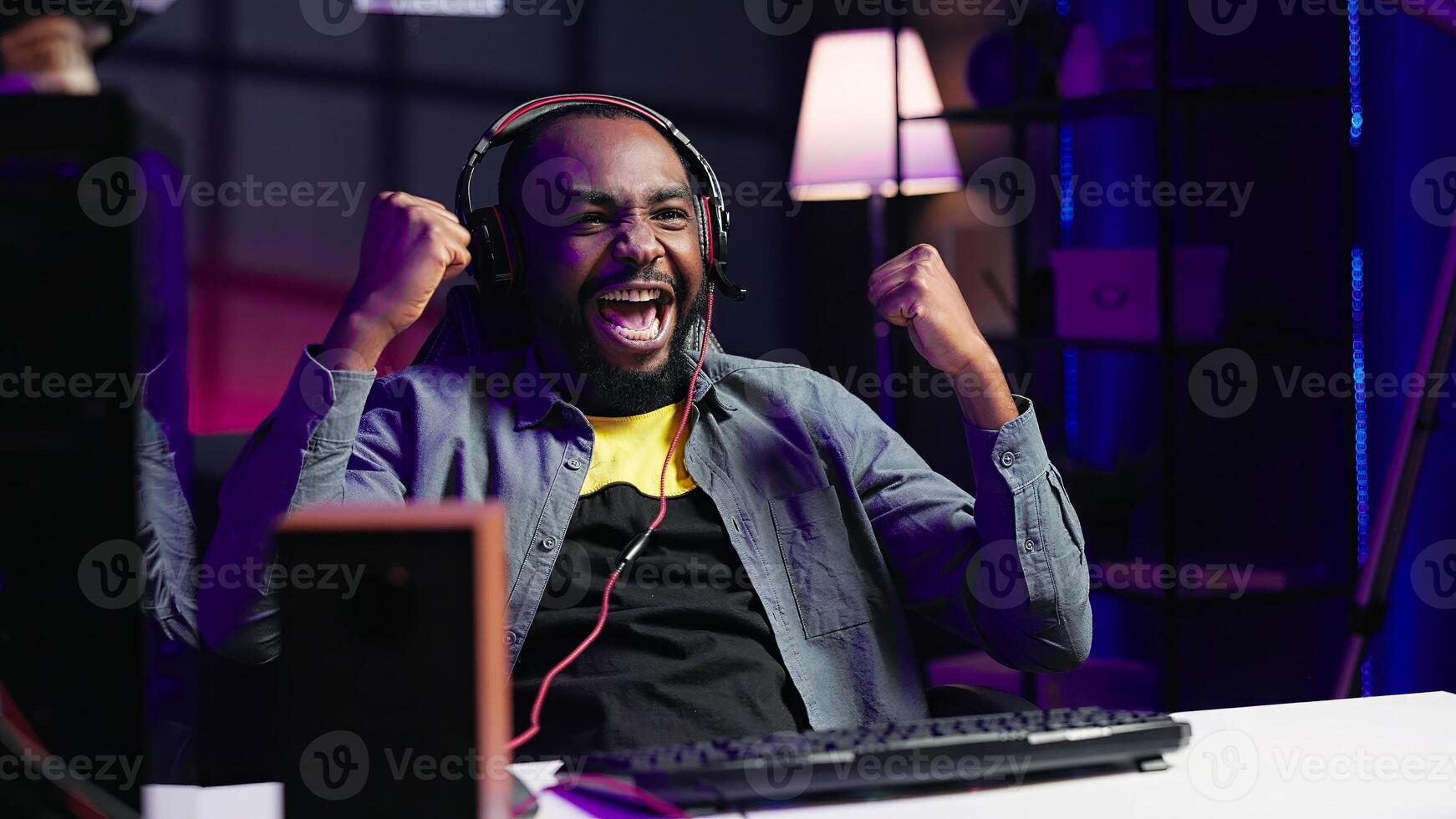 Merry man feeling happy while playing videogames on gaming PC, celebrating victory. Player excited after winning computer game, displaying happiness emotions, shaking fist, camera A photo