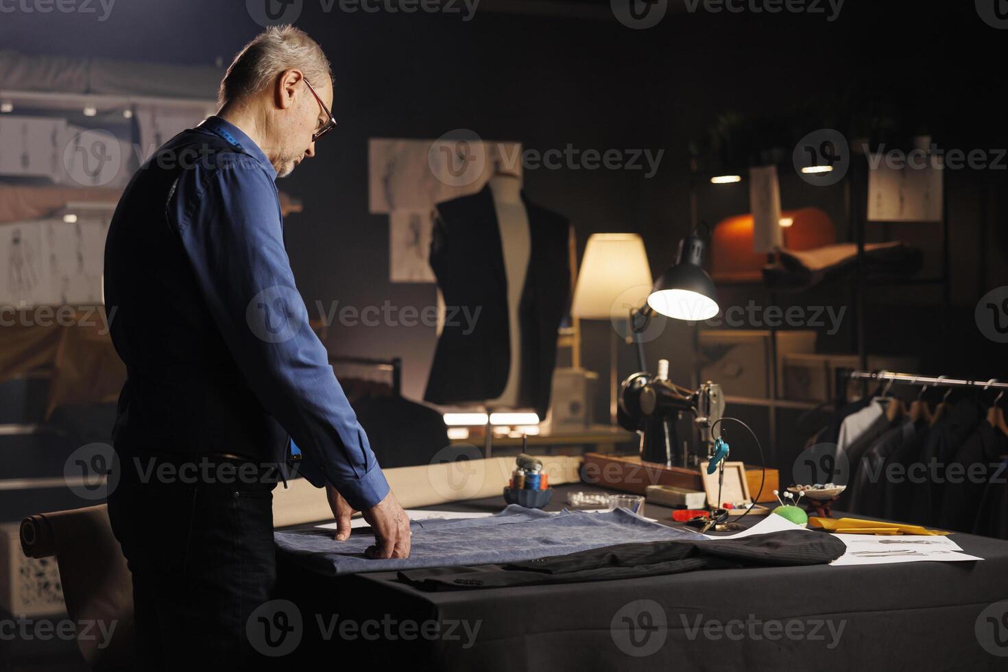 Elderly expert suitmaker alone in professional tailoring studio, designing upcoming fashion collection. Senior craftsman in atelier shop workspace manufacturing premium quality clothing photo