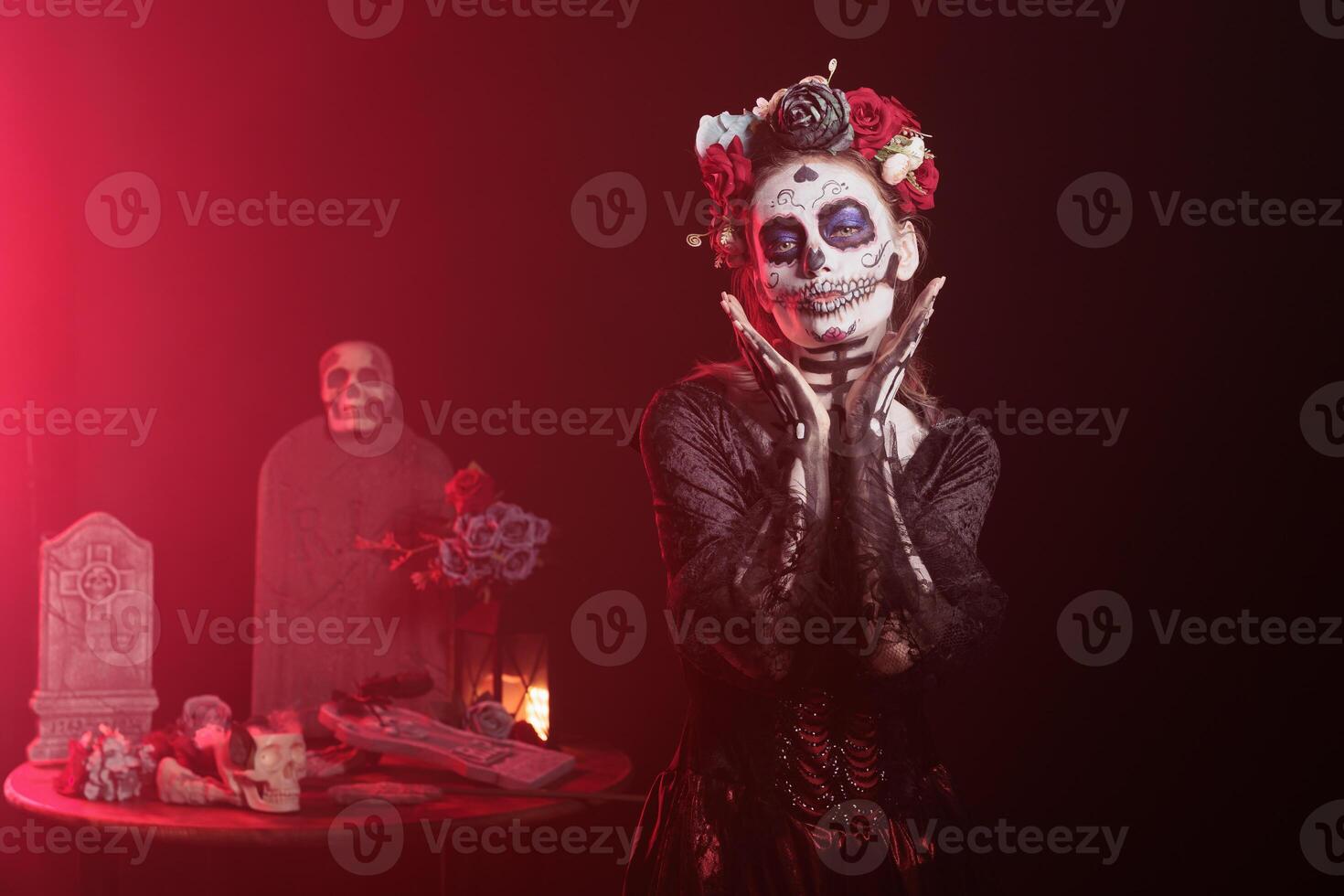 Woman in occult decorated studio during Day of the Dead Halloween event honoring dead loved ones. Scary lady doing ancient Aztec custom of celebrating ancestors, red light background photo
