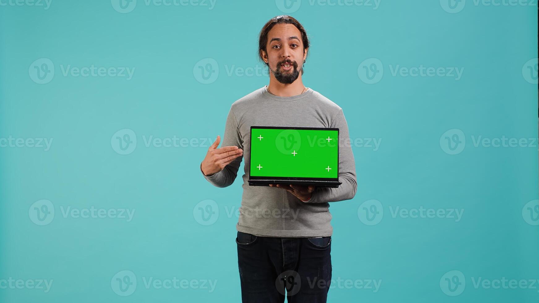 Man presenting green screen mobile laptop, isolated over studio background. Arab person holding copy space chroma key notebook device used for advertising brands, camera A photo