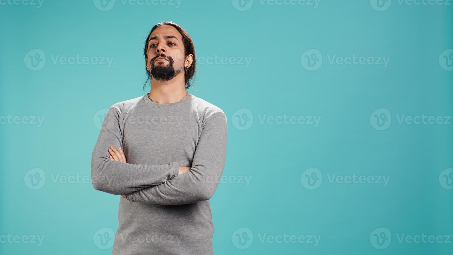 Grumpy man with sulking facial expression crossing arms, feeling annoyed, isolated over studio background. Portrait of irate person in bad mood feeling frustrated after argument, camera B photo