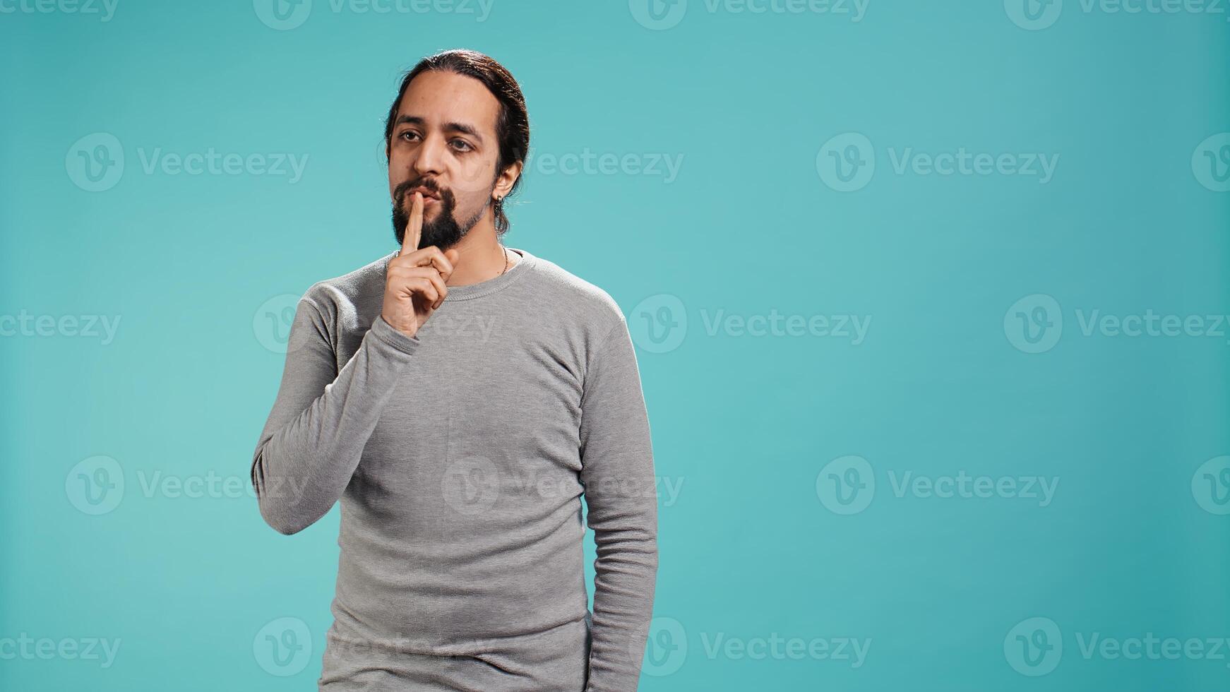 Annoyed man doing shushing hand gesturing, irritated by noise, having negative mood. Person placing finger on lips, doing quiet sign gesture, isolated over studio background, camera B photo