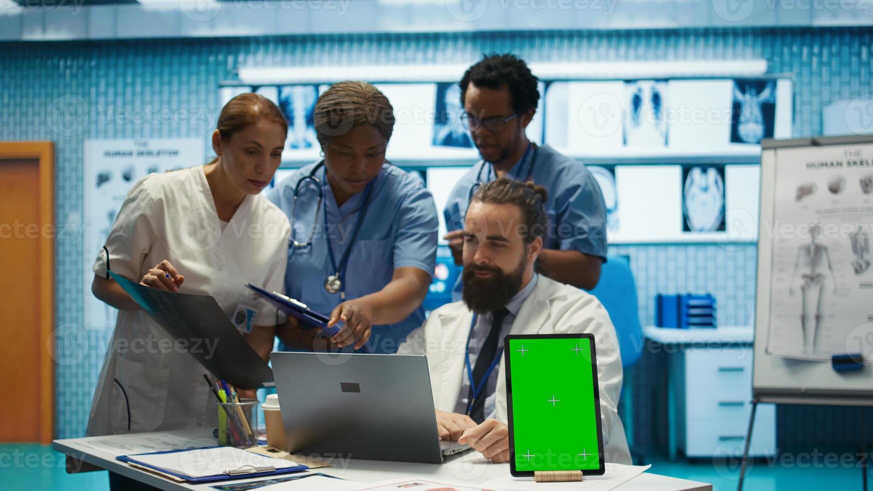 Group of doctors consulting hospital records next to chroma key display, using x ray test results to examine diagnosis. Diverse experts meeting at private clinic to provide treatment plan. Camera B. photo