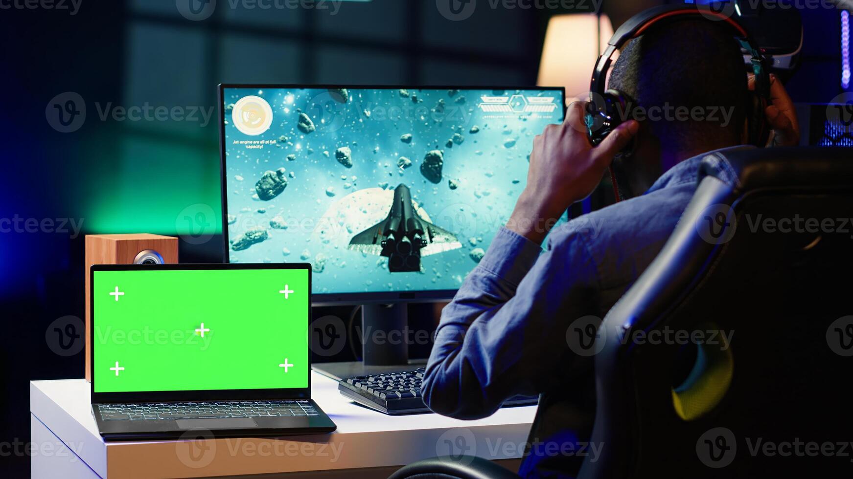 Mockup laptop next to man playing high FPS singleplayer videogame with spaceship shooting lasers. Isolated screen notebook near gamer using crosshair to hit targets in SF game photo