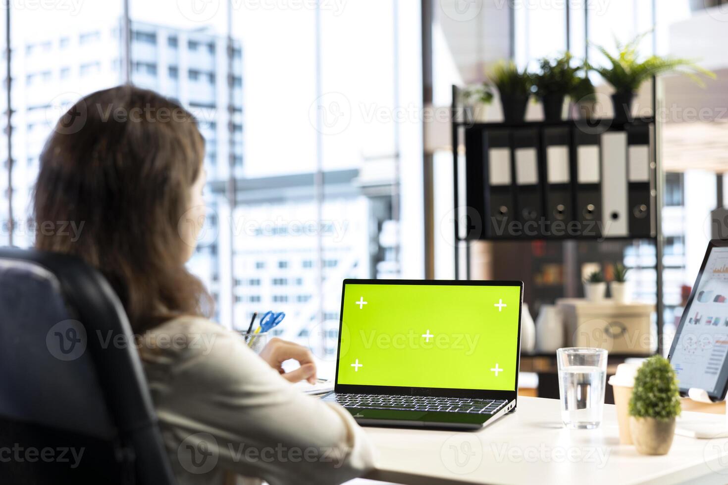 Business director working in her own office with green screen, looking at device display and developing a new project idea. Female entrepreneur empowered by corporate culture. photo
