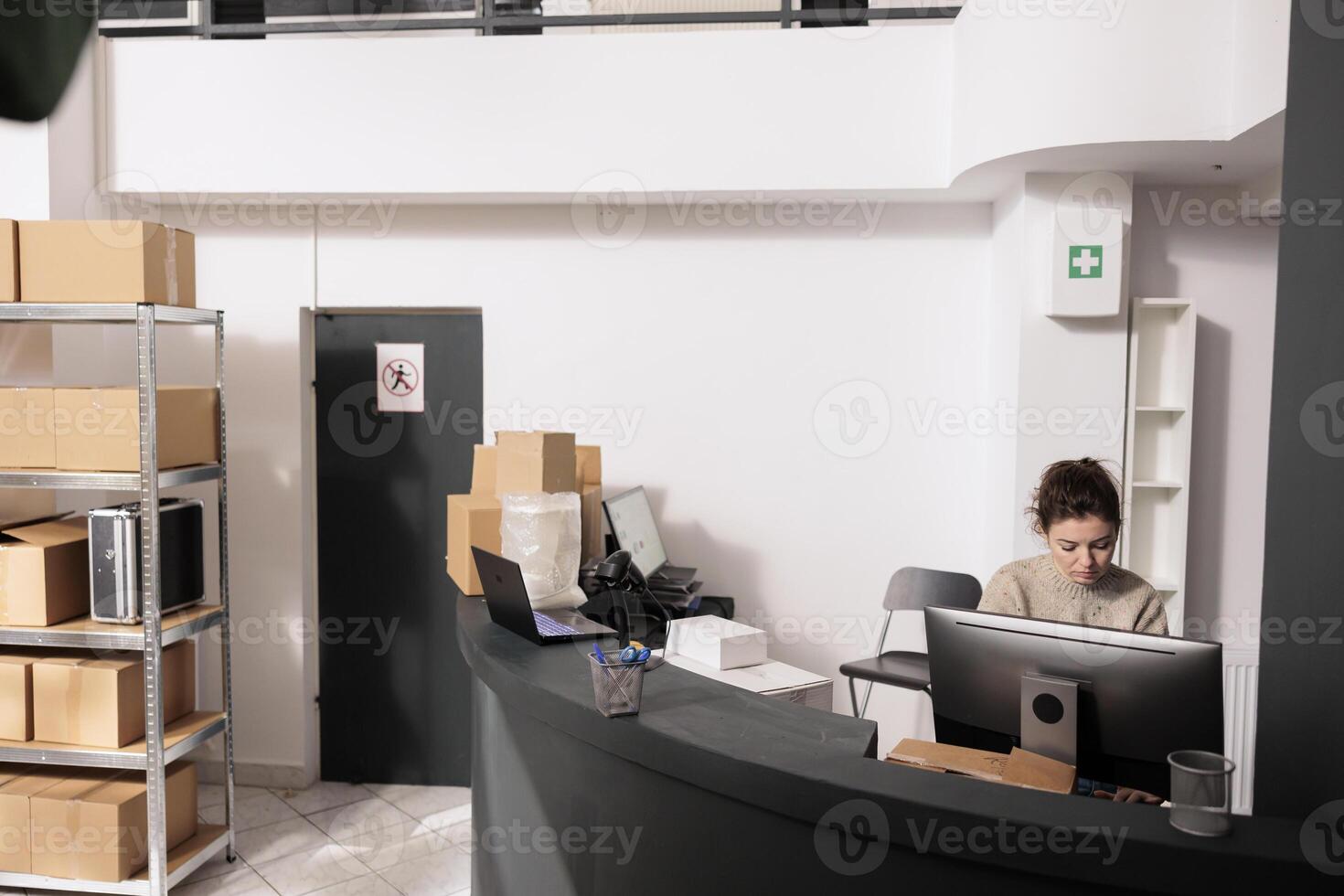 Storehouse manager standing at counter desk checking shipping details on computer before start preparing customers orders. Woman supervisor working at merchandise inventory report in storage room photo