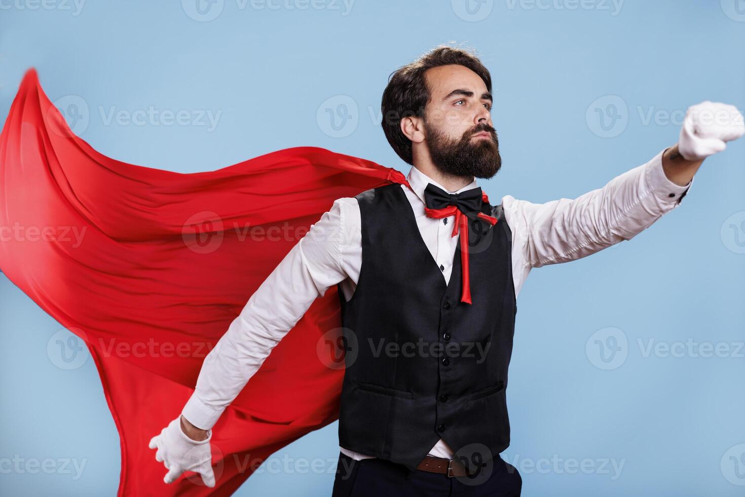 Strong character with fantasy cape standing in studio with blue background, acting confident and determined on camera. Powerful person presenting dedication to protect citizens. photo