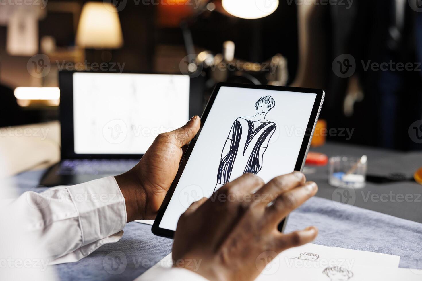 Couturer meticulously analyzing drawn sketch designs on tablet of exquisite dress comissioned by woman. Dressmaker checking last finishing details of upcoming sartorial custom handmade attire photo