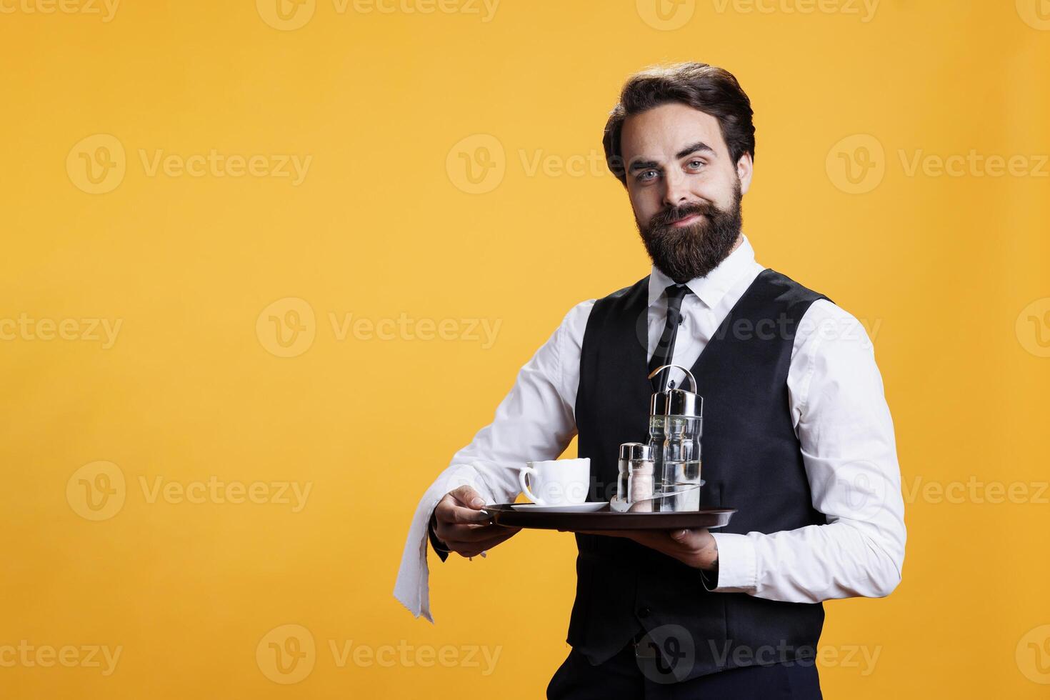 Stylish waiter carrying tray with coffee and cutlery to serve people at five star restaurant, luxurious catering employee with towel over arm. Professional butler with suit and tie holds platter. photo