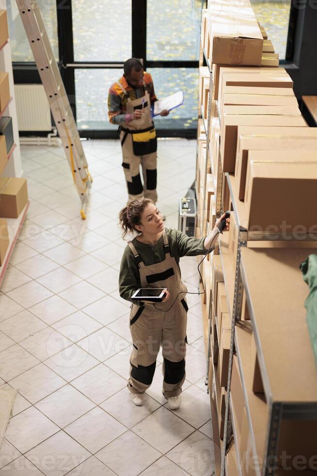 Small business manager scanning boxes barcode using store scanner during warehouse inventory, checking products list on tablet computer. Employee preparing online clients order in storehouse photo