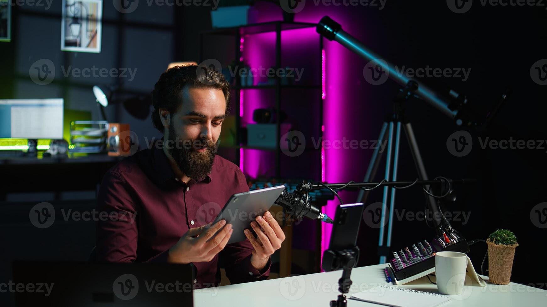 Tech specialist presenting tablet in entry level low budget price range to interested viewers, filming with smartphone on tripod. Man reviewing digital device, recording with mobile phone, camera B photo