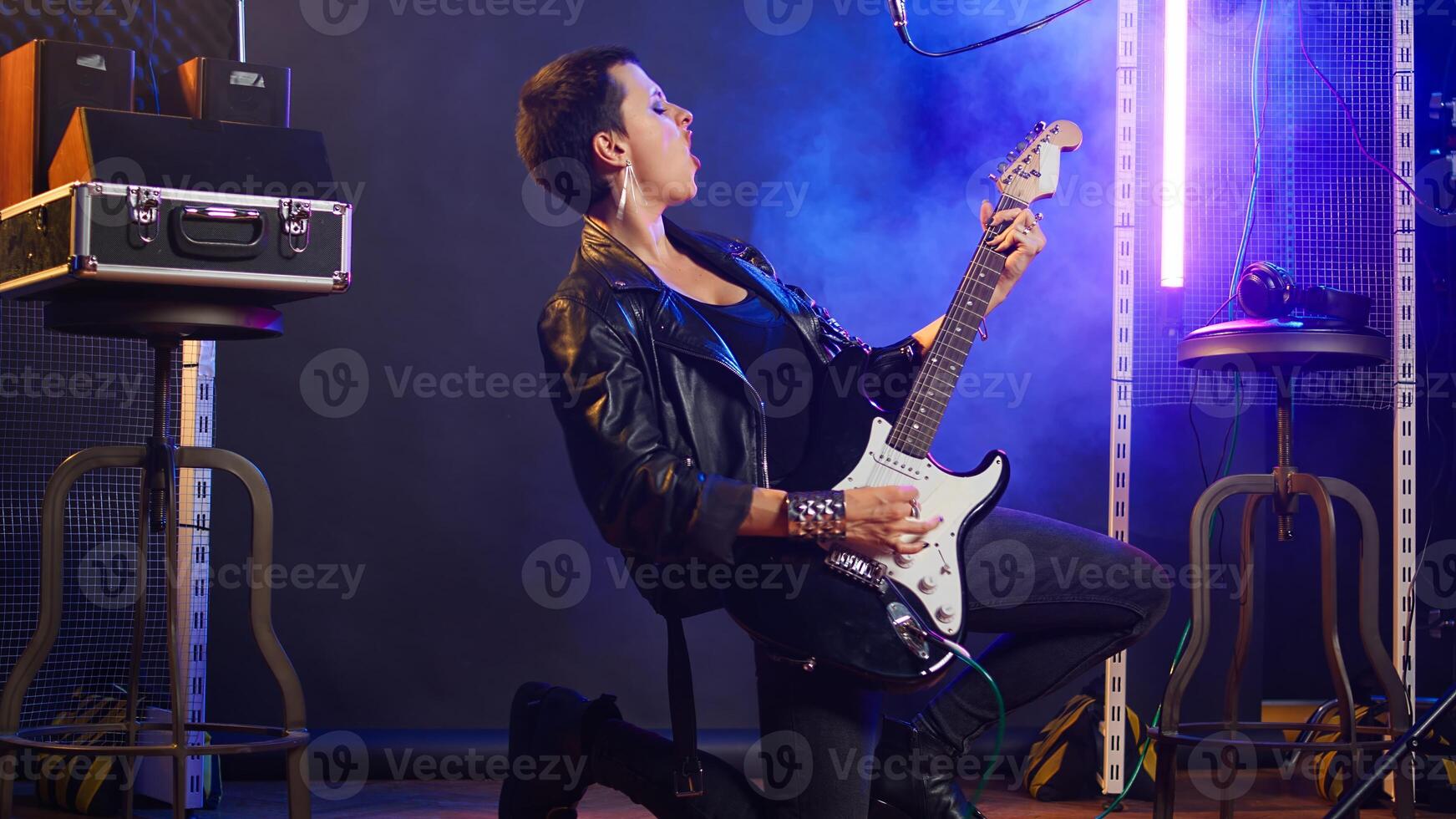 Female musical performer in a leather jacket plays electric guitar, delivering a fierce energetic music performance that captivates audience with her bold grunge style. Music lover. Camera A. photo