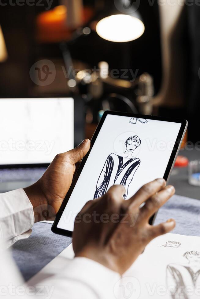 Dressmaker checking last finishing details of upcoming fashion bespoke handmade outfit. Tailor meticulously analyzing drawn sketch designs on tablet of exquisite dress comissioned by woman. photo