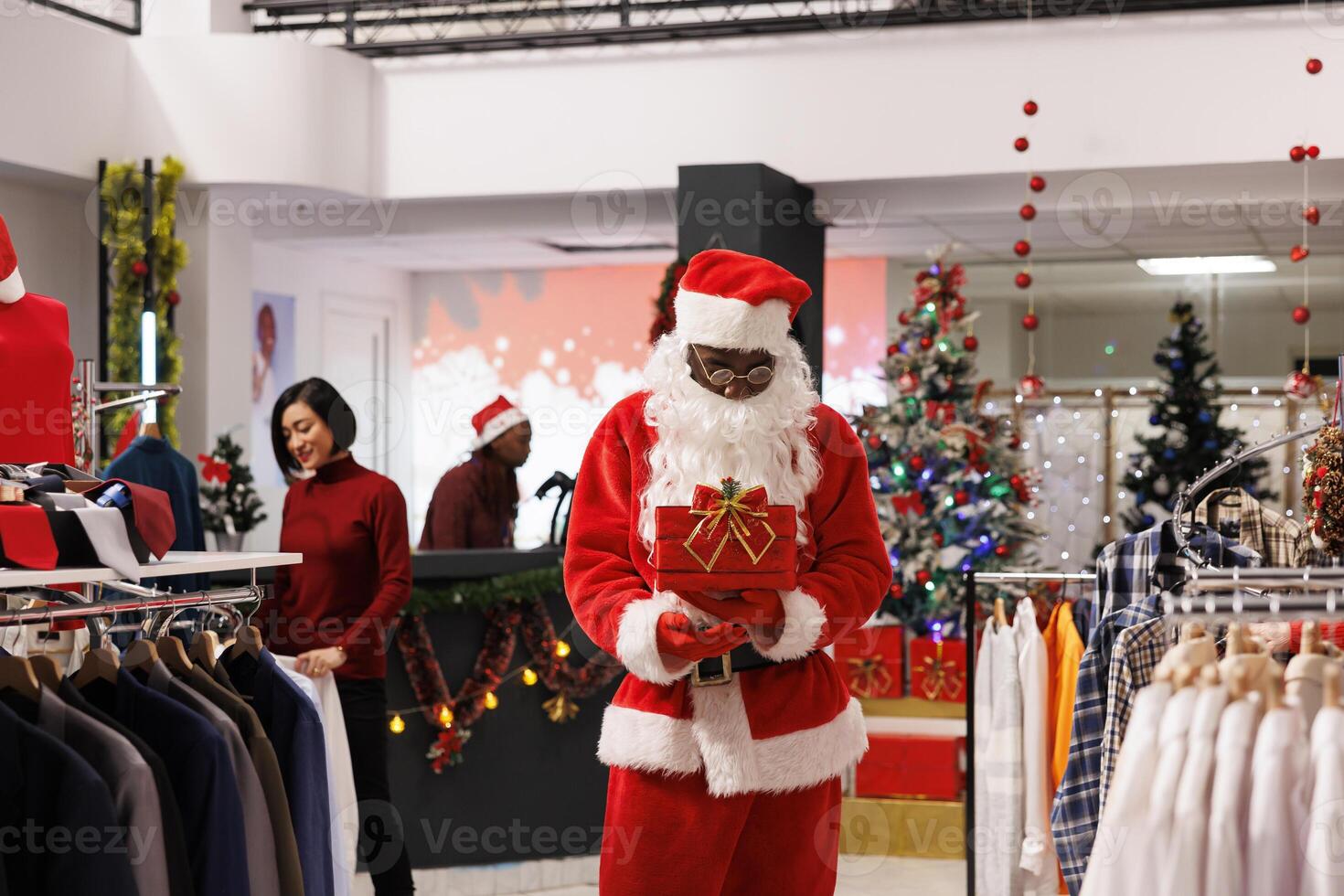 Employee drawing contest winners in store, presenting names of participants from red raffle box. African american man in santa claus costume greeting customers at prize drawing. photo