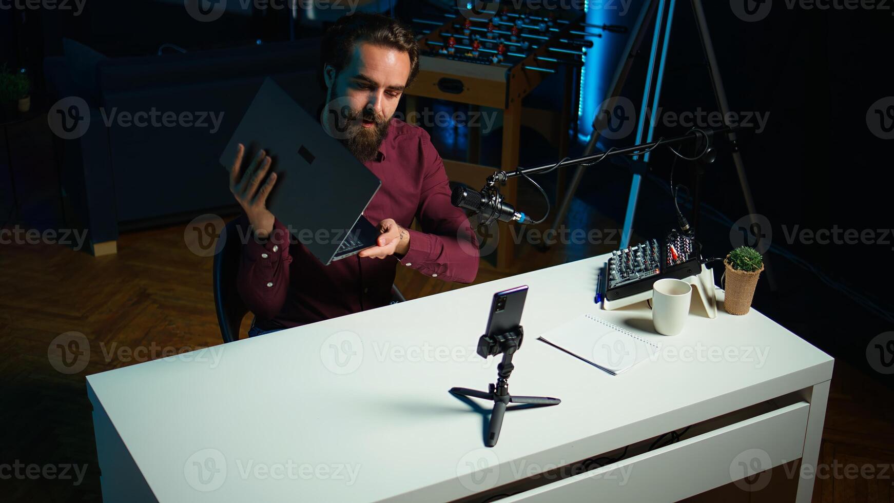 Tech expert assessing laptop performance, talking about components used inside, filming with smartphone. Entertainer reviewing notebook on technology internet channel, recording with phone, camera B photo