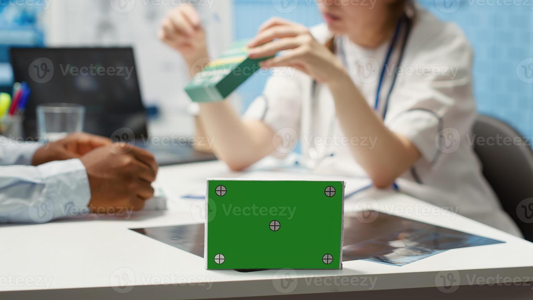 Patient and medical specialist at a check up visit next to green screen on medicine box, discussing about treatment and medical drugs for recovery. Female doctor pointing at medicaments. Camera A. photo