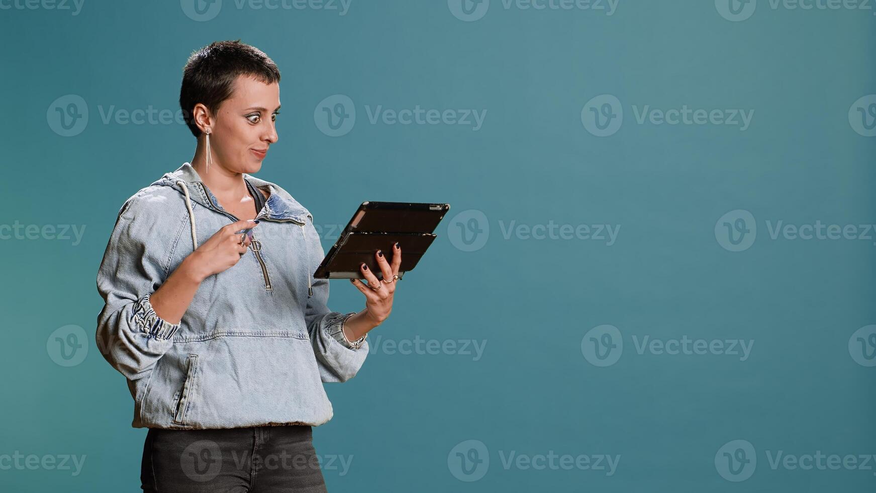 Stylish person doing online shopping with her credit card in studio, feeling happy spending money on what she likes. Catching seasonal promotions for placing multiple orders, e commerce. Camera B. photo