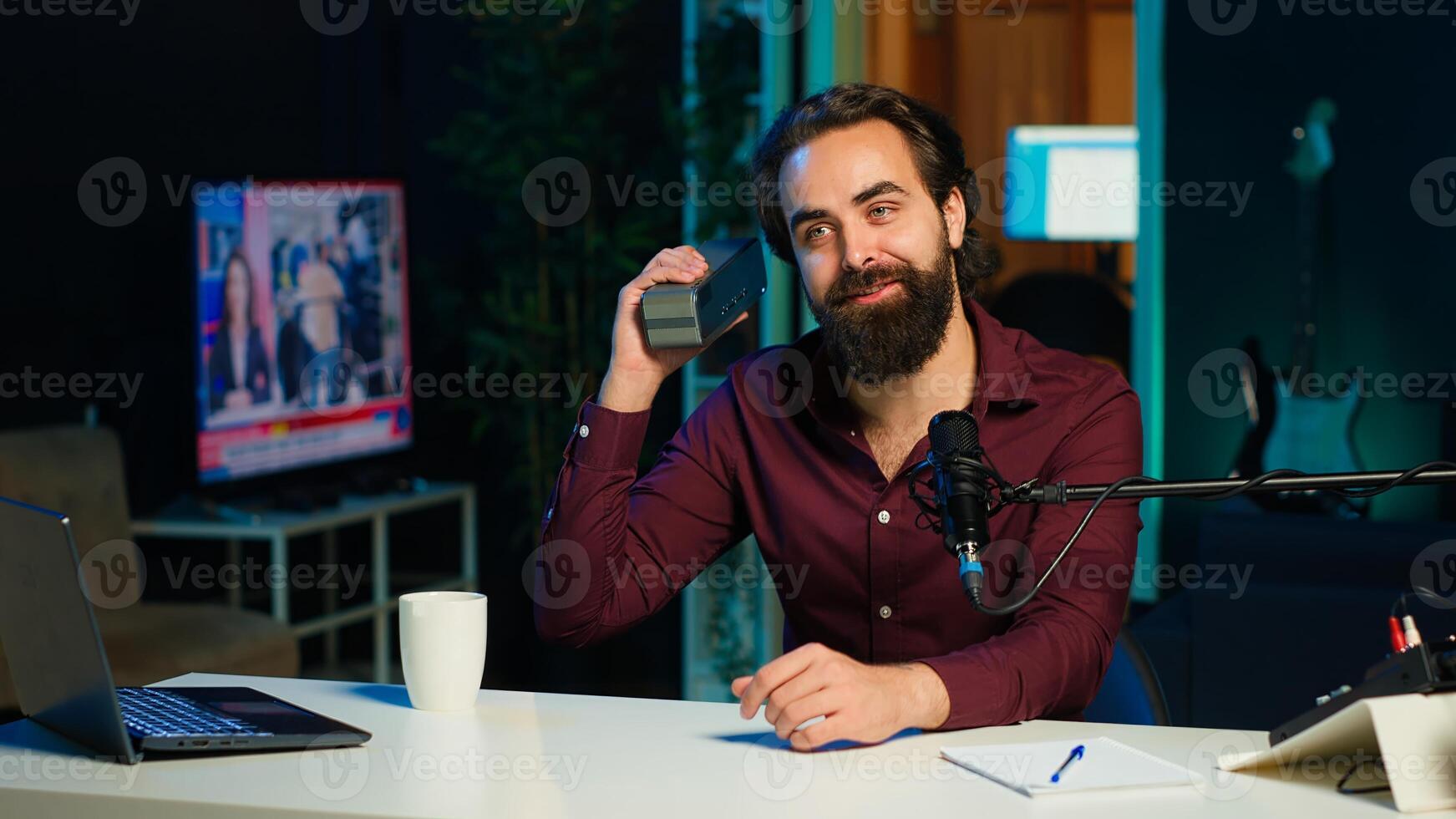 Smiling media star doing technology review of wireless portable speaker for online platforms channel. Cheerful influencer presenting music playing device to his audience, camera A photo