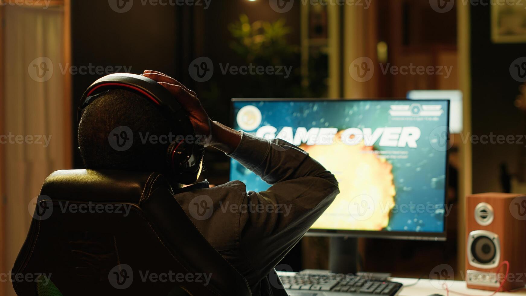 Heartbroken gamer dejected after losing in online multiplayer videogame, being defeated by rivals. Man putting hands on head in frustration after seeing game over screen on gaming pc monitor, camera A photo