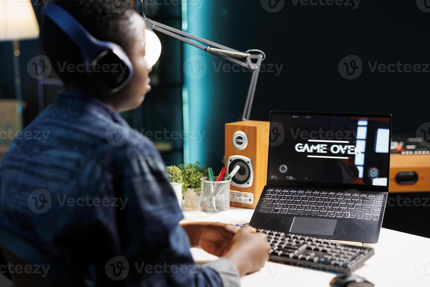 African american woman with headphones sits in front of her personal computer that is displaying game over. Female gamer wearing a headset, losing a game is staring at her digital laptop screen. photo