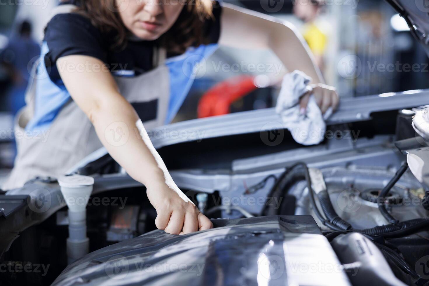 Adept engineer in garage finishing fixing car, looking underneath vehicle hood to remove remaining oil leaks. Worker does routine radiator cleaning on client automobile in auto repair shop photo