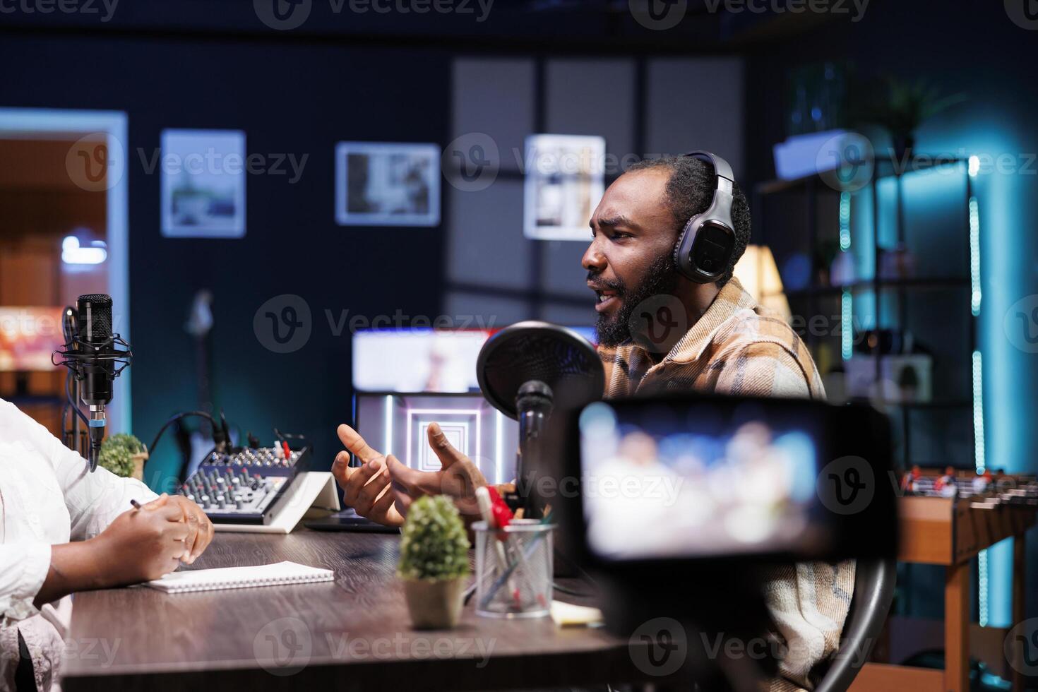 Male presenter filming a live talk show at home with high quality camera. African American man is wearing headphones and speaking into microphone during internet production for podcast episode. photo