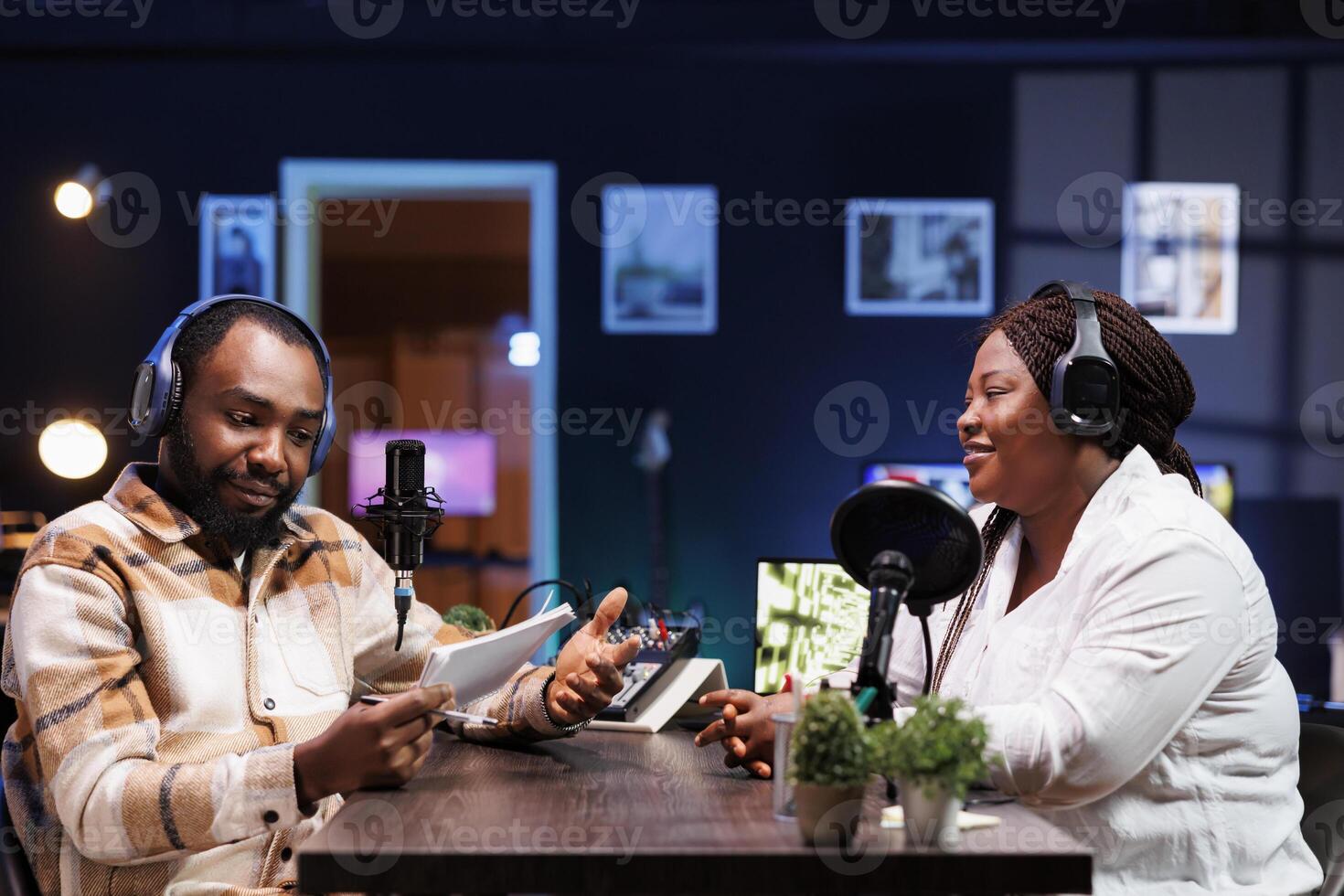 African American podcast host interviews a female content creator in a neon-lit home studio using advanced recording equipment. Their engaging discussion is broadcast digitally to their online fans. photo
