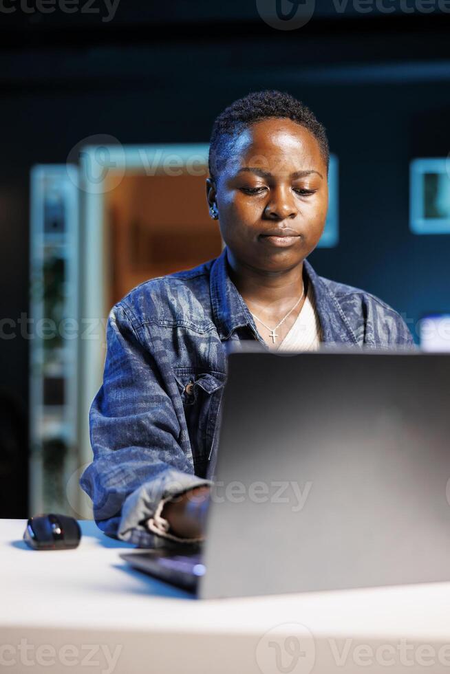 Portrait of focused african american student typing on digital laptop, working on her thesis project. Dedicated black female freelancer reviewing financial projections of company on personal computer. photo