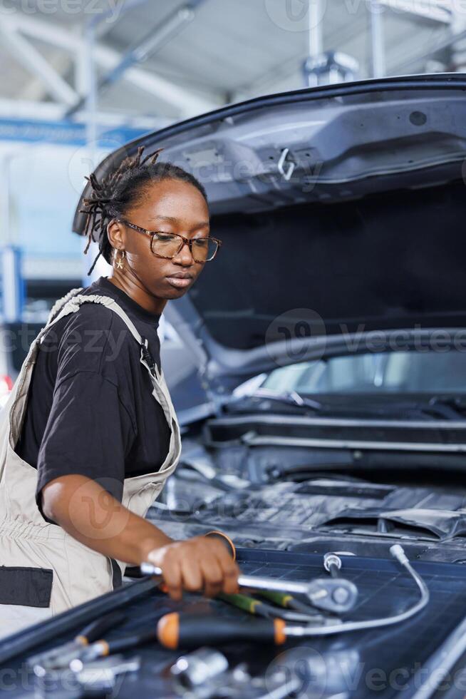 Mechanic in car service picks torque wrench from work station bench, using it to tighten bolts after replacing fuel tank. Licensed BIPOC garage worker uses professional tools to fix client automobile photo