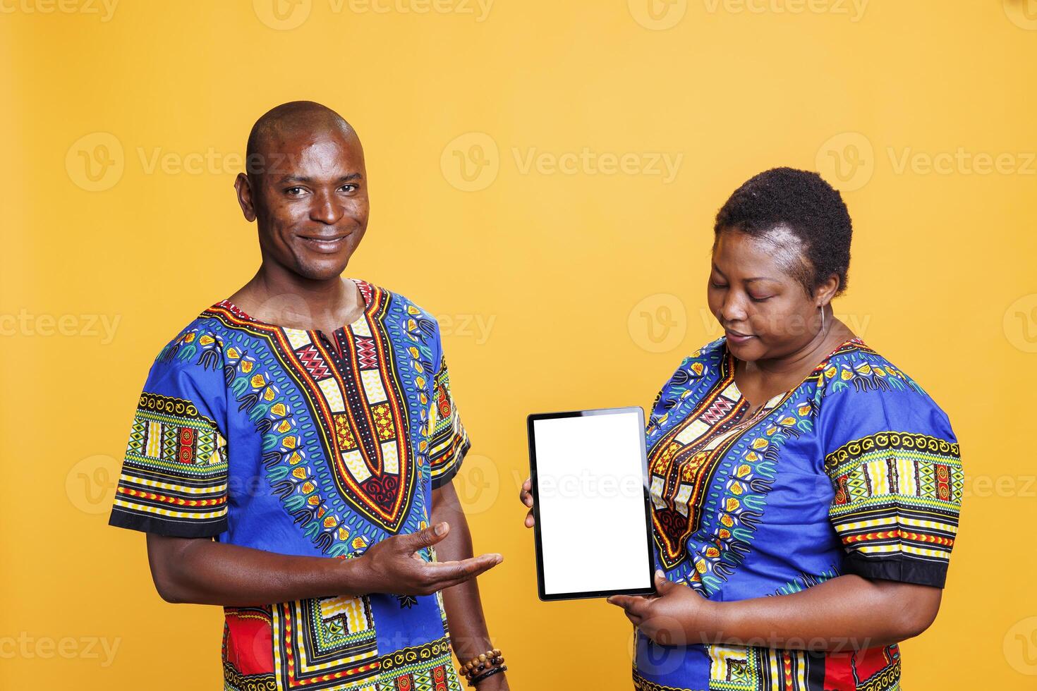 Black man and woman advertisers holding digital tablet with white screen, presenting new portable gadget. Smiling couple showcasing device with blank touchscreen mockup and looking at camera photo